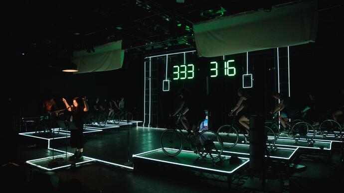10 cyclists pedal on set in the rehearsal room for A Play for the Living in a Time of Extinction