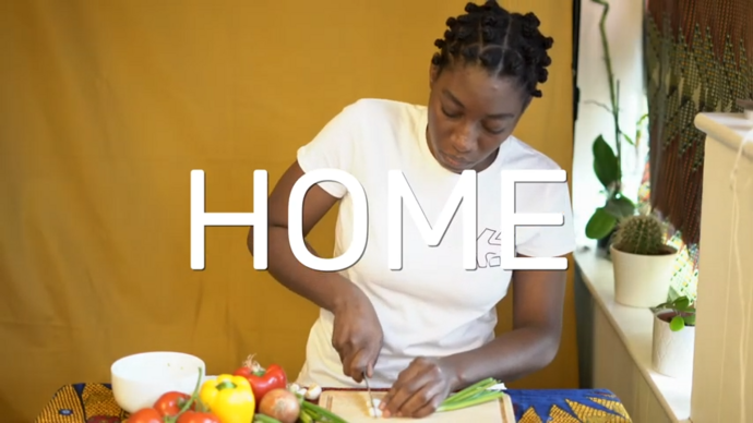 An image of Julene Robinson performing in the kitchen of their house against a yellow background. 
