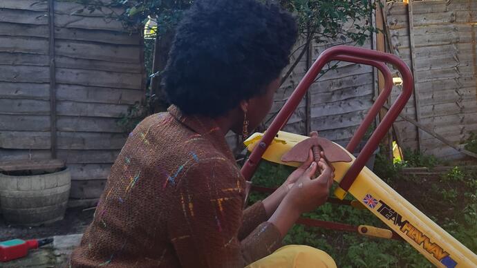 Adanma is in a garden sitting and painting a slide