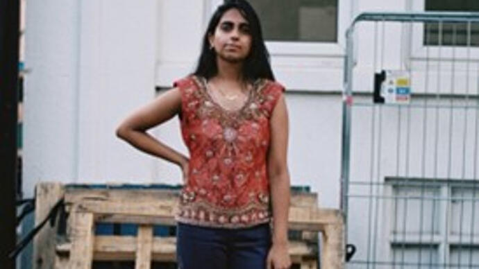 A woman in a red top standing in front of wooden palettes and a white door.