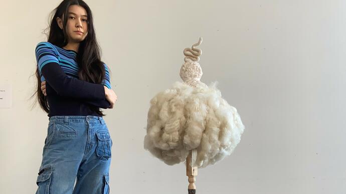 One person wearing jumper and blue jeans stands next to their sculpture