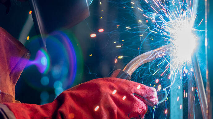 Performance artist Rachel Mars welds a metal gate while wearing a protective helmet