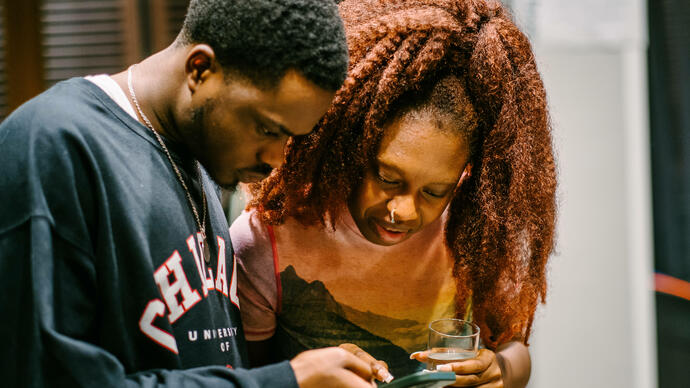 two people standing together looking down at a phone