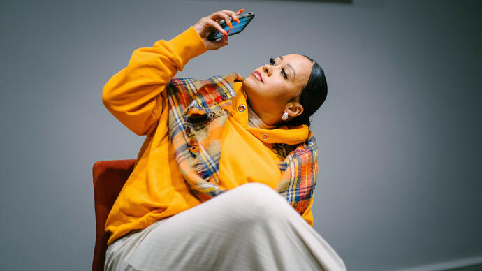 Lady in yellow jumper looking up and taking picture on phone