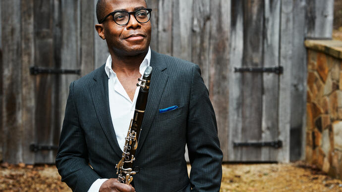 Anthony McGill standing in front of a wooden barn holding his clarinet