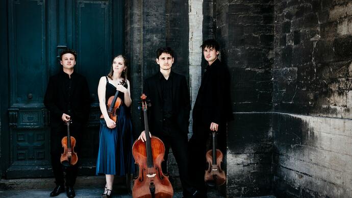 The Sonoro Quartet standing in front of a stone wall and large blue door, holding their instruments