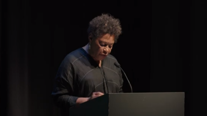 carrie mae weems stands behind a lectern