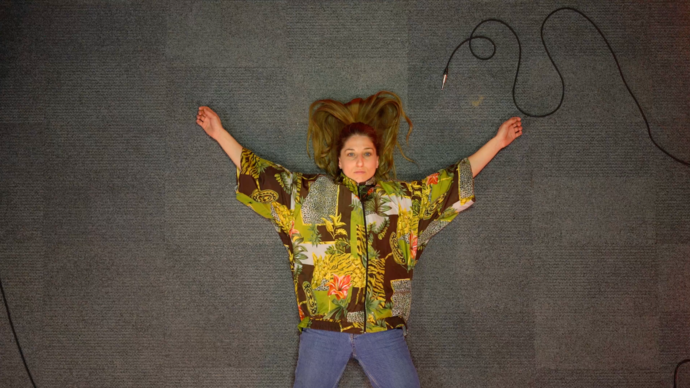 A dancer lies on the floor wearing a colourful top. Their arms are outstretched.