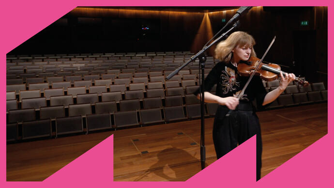 Fenella Humphreys playing her violin on stage in an empty Milton Court Concert Hall, with triangular pink shapes forming a border around the image