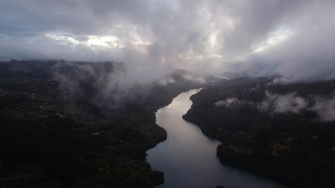 Still from Mat Collishaw's Sky Burial film, of a large river running through a forested landscape, with clouds swirling above