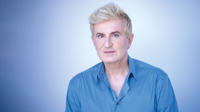 Jean-Yves Thibaudet wearing a blue shirt, in front of a sky blue background