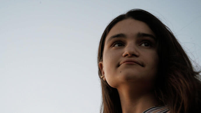 A woman looks into the distance against a sunset 