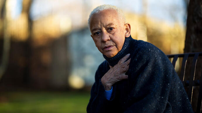 Photo of Nikki Giovanni in her garden, sitting on a bench.