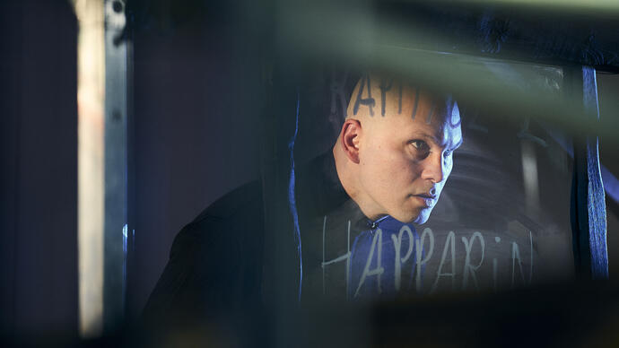 Director Bui Dam performs as a shadow actor. He stands and stares through a sheet of glass that has Faroese writing on it.