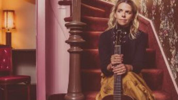 Aoife O'Donovan sits on purple staircase holding guitar