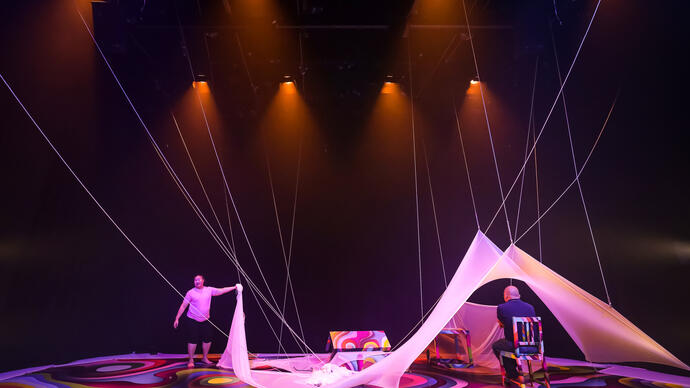 Two performers move around a floor with bright circles, in and between white draping fabric.