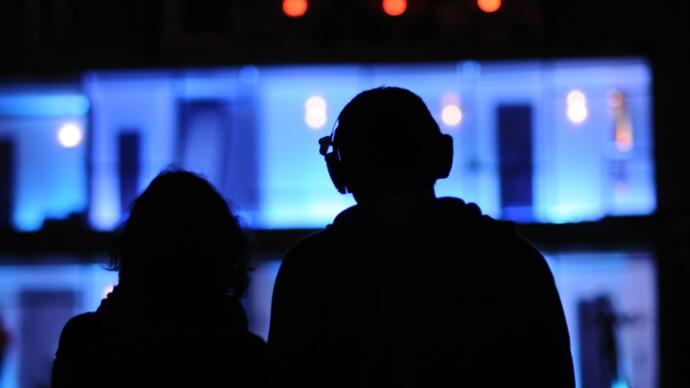 The silhouettes of two people watching something on screen.