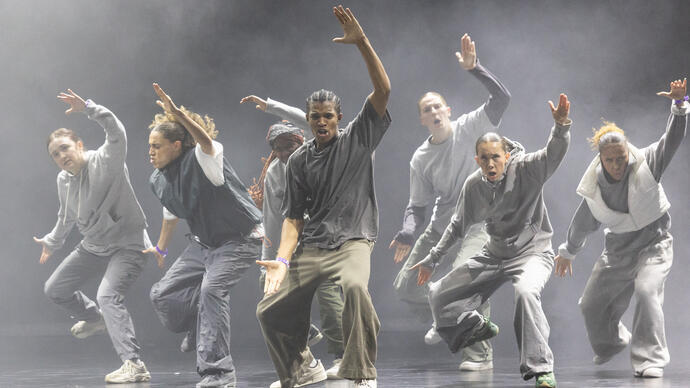 A group of hip hop dancers caught in motion. They lift one arm in the air and open their mouths.