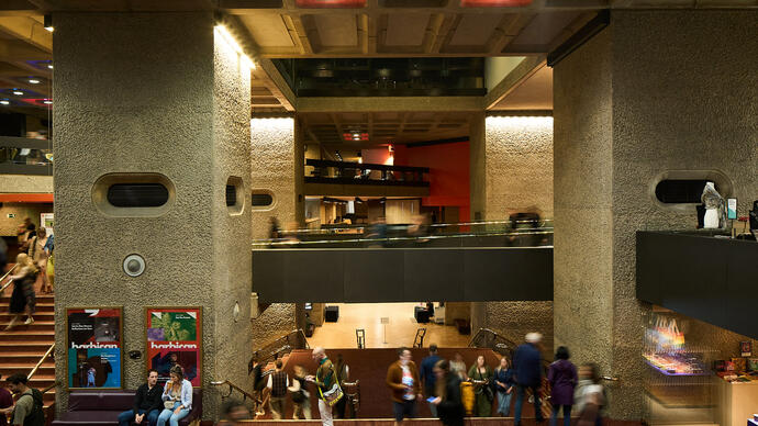 A candid photograph of lots of people sitting or standing in the Barbican Mezzanine foyer