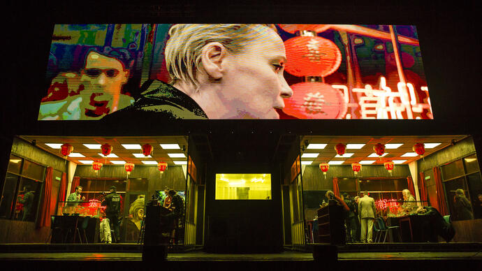 1. A large screen displays a woman as different scenes in a Chinese restaurant unfold on stage