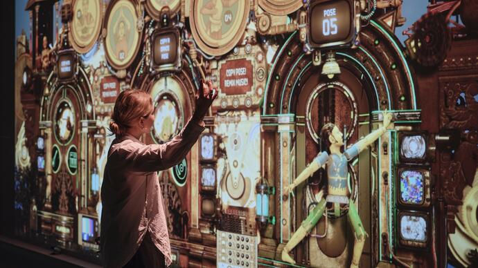 A woman stands in front of a large wall projection, copying the dance move shown by the character on the screen