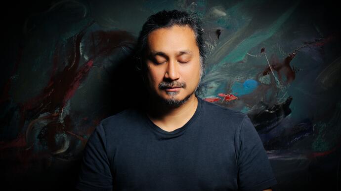 Headshot of an Asian man against a dim colourful background