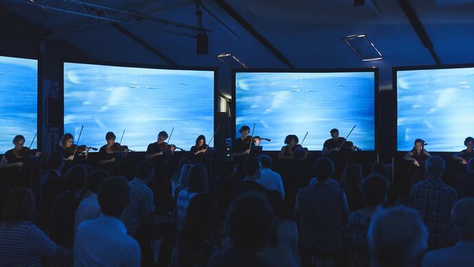 A small quartet performing in front of an audience with four screens behind them