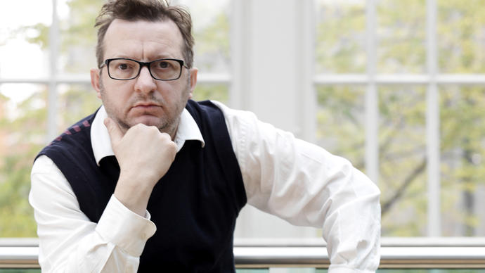 A photo of Mark-Anthony Turnage who has written the music for Coraline. He is wearing a white shirt and black vest.