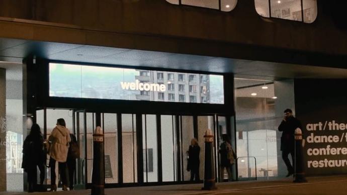 an amazing photo of the barbican centre entrance at night with some visitors waiting to go see a show in central london