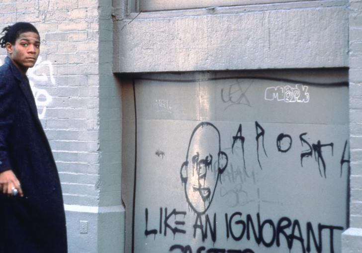 Photo of Basquiat standing by graffiti