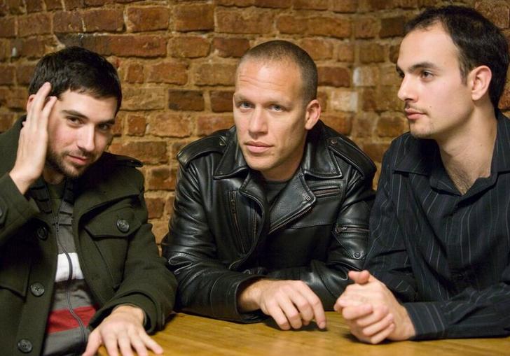The Avishai Cohen trio wearing dark jackets sitting at a wooden table