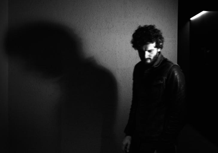 A black and white photo of Apparat in front of a wall, his shadow is cast on the wall behind him