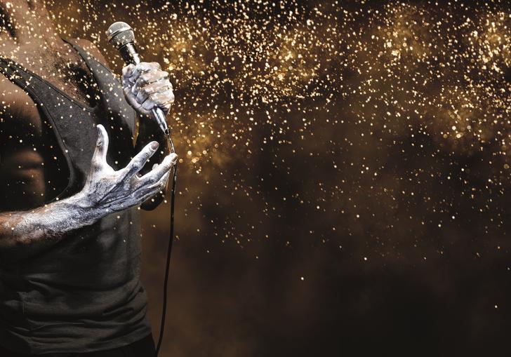zoomed in image of a man's chest with a vest on. One hand grips a mic and the image is full of glitter 