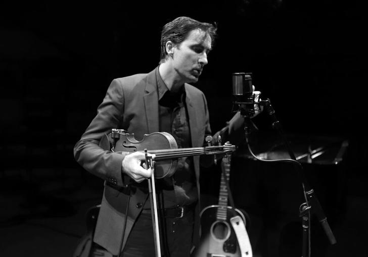Andrew Bird holding his violin and singing into a microphone