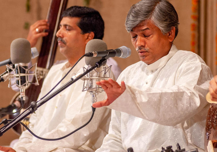 The Gundecha brothers wearing white and singing into microphones