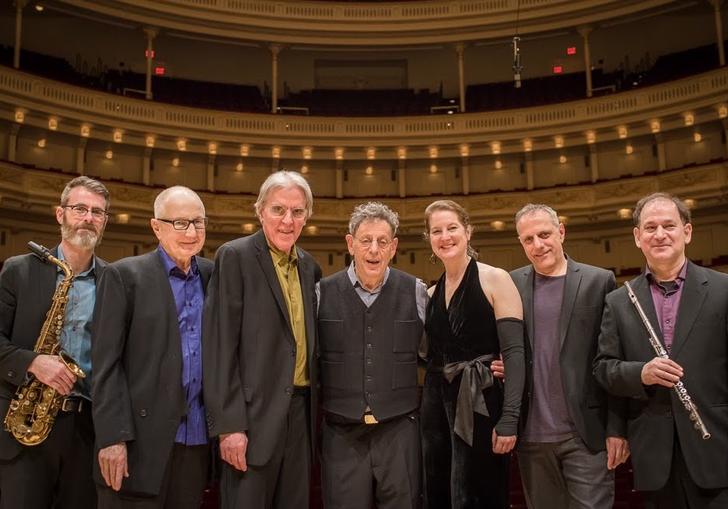 The Philip Glass Ensemble with Philip Glass pose for a photo in a concert hall
