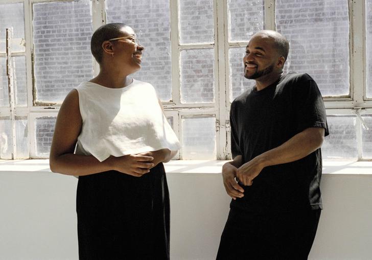Cecile McLorin Salvant and Sullivan Fortner leaning on a ledge in front of windows with sun streaming in