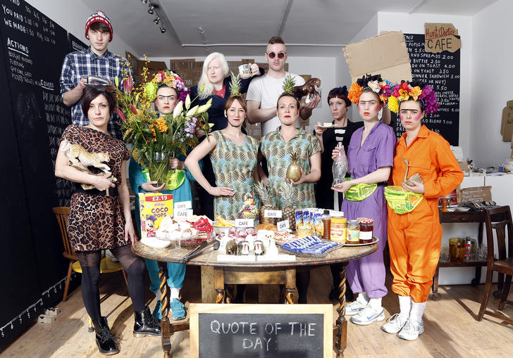 A group of people standing in a huddle around a circle table, wearing elaborate oufits.