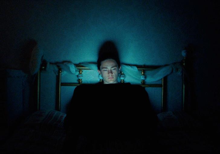 someone sitting alone in a dark room on their bed with the light of a computer screen in their face