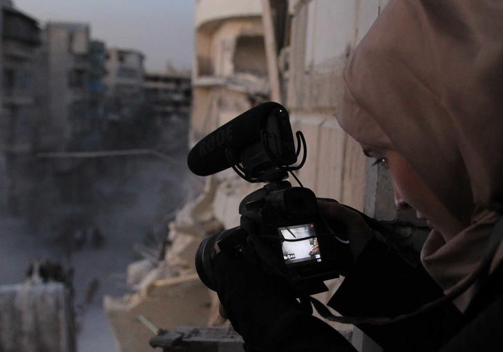 Waad with a camera pointing down to the street which is covered in dust and rubble
