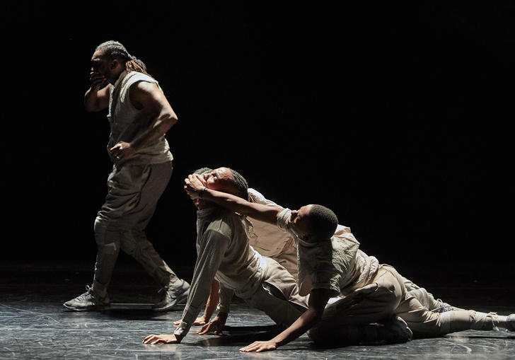 Four dancers on a stage. One is covering their own mouth while two others cover another's mouth