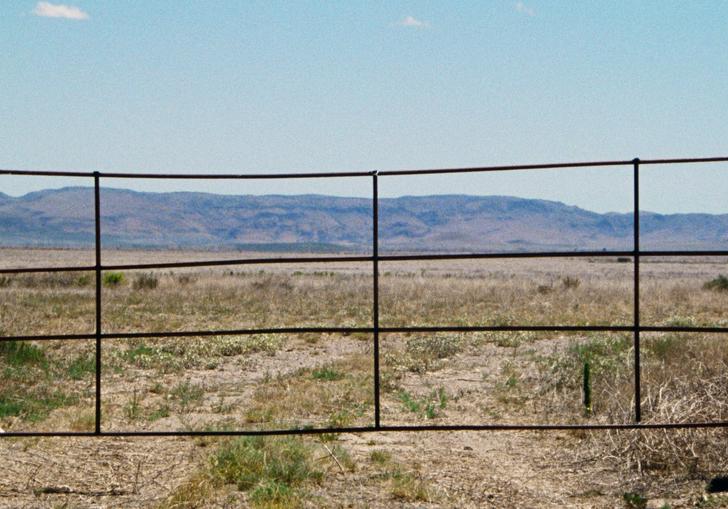 a fence set against a desert like backdrop with mountains and blue sky