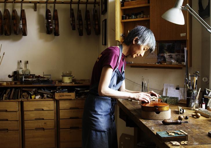 image of a man in an art atelier working on a violin. There are many tools hanging around