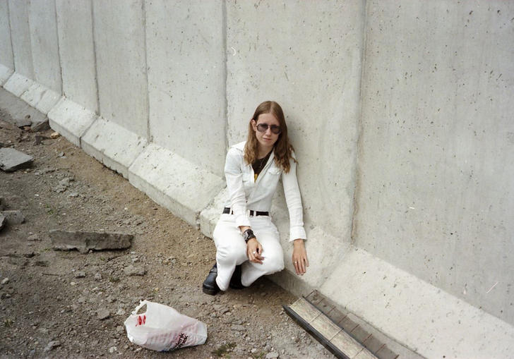 Woman dressed in white crouching next to the berlin wall