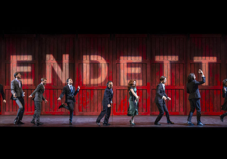 Ten people stand in various poses in front of a red wall which spells out 'vendetta' 