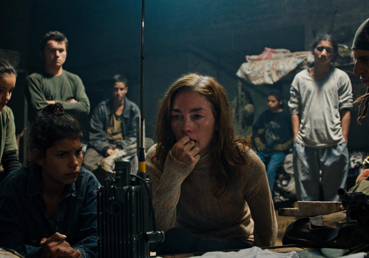 A young woman and some children wait attentively at a radio in the film Monos