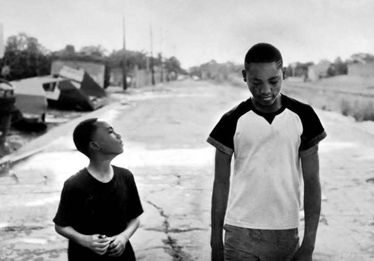 two boys walking down the street in black and white