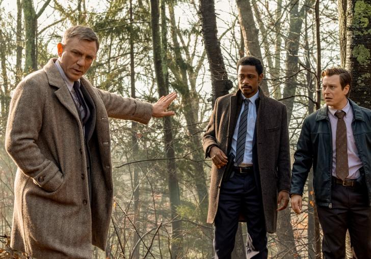 Daniel Craig in a cream overcoat stands in the woods with Lakeith Stanfield, in Rian Johnson's Knives Out
