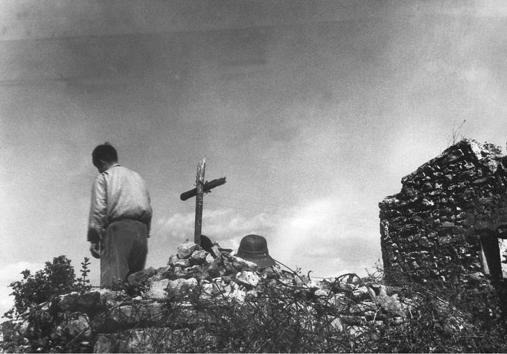 A black and white image of a boy with his back to the camera, by a makeshift grave