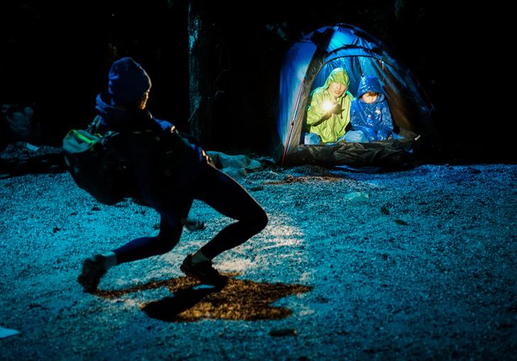 Two children cowered in a tent, a man in front of them is posed like he is falling backwards, bent at the knee